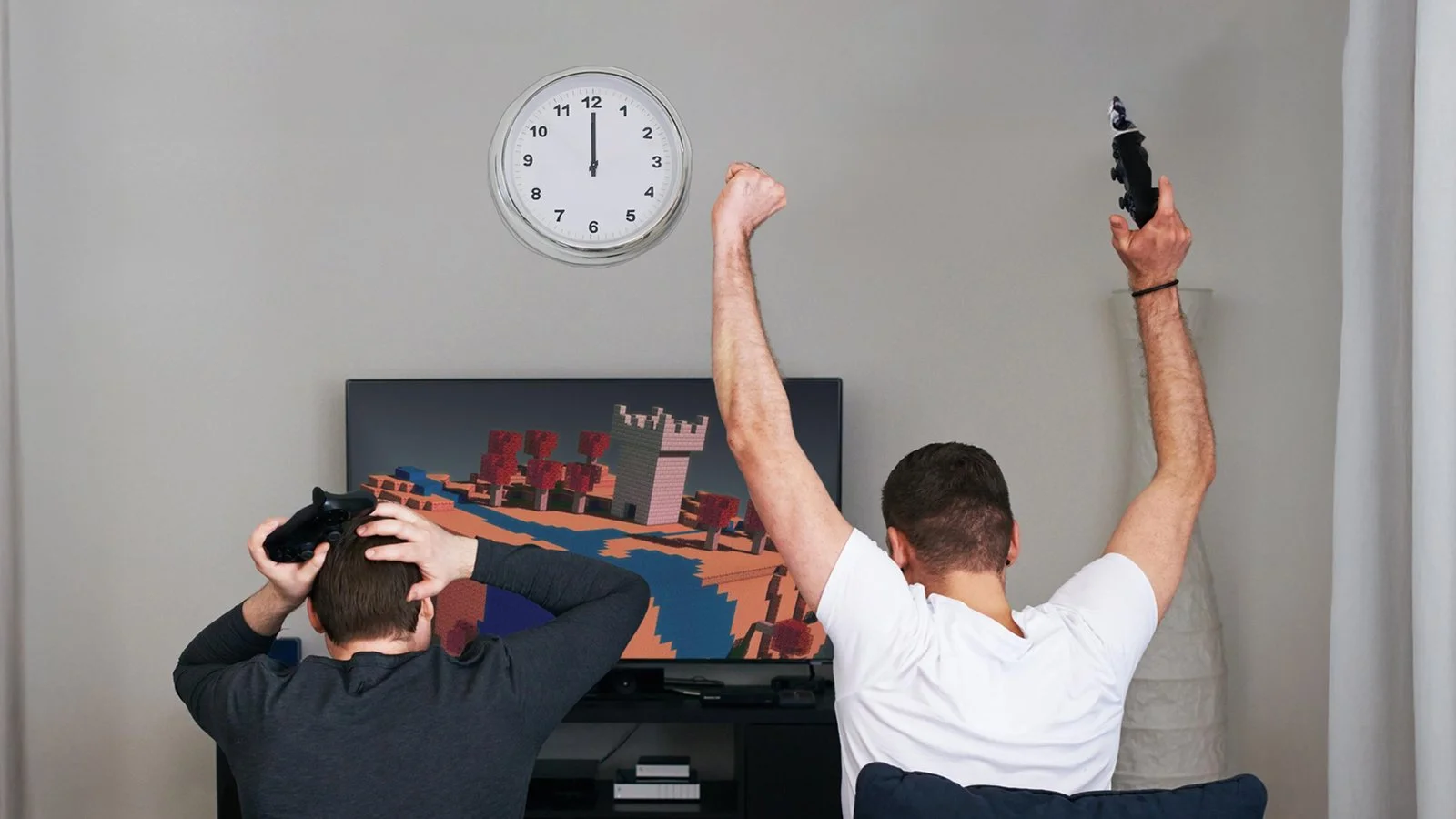 Duvar saatinin altında televizyon karşısında oyun oynayan iki genç; biri sevinçle kollarını kaldırmış, diğeri ellerini başına koymuş