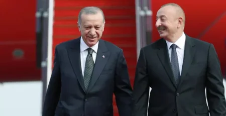 Kırmızı halı ve uçak merdiveni önünde gülümseyerek yan yana yürüyen takım elbiseli iki adam
