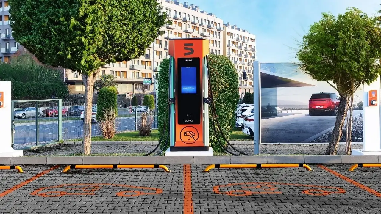 Ağaçlar ve binalar arasında, otoparkta duran turuncu-siyah elektrikli araç şarj istasyonu