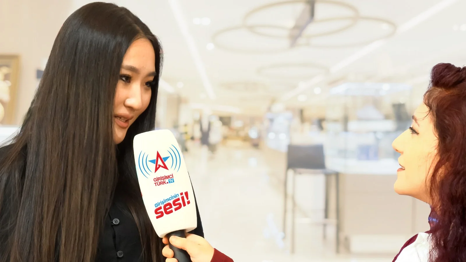 Mikrofon uzatılan uzun saçlı genç bir kadın ile röportaj yapan muhabir