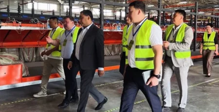 Fosforlu yelekli çalışanlar eşliğinde lojistik merkezini gezen takım elbiseli yetkililer