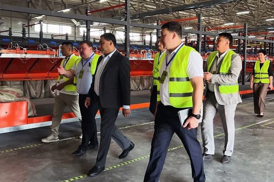 Fosforlu yelekli çalışanlar eşliğinde lojistik merkezini gezen takım elbiseli yetkililer