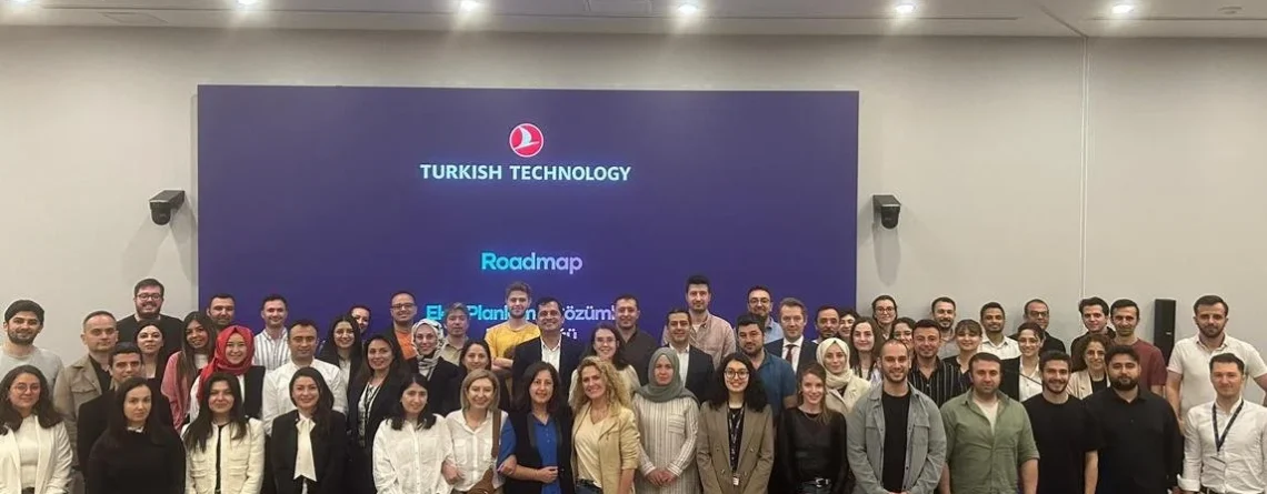 Turkish Technology logolu ekranın önünde, renkli koltukların arkasında poz veren kalabalık bir katılımcı grubu