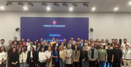 Turkish Technology logolu ekranın önünde, renkli koltukların arkasında poz veren kalabalık bir katılımcı grubu