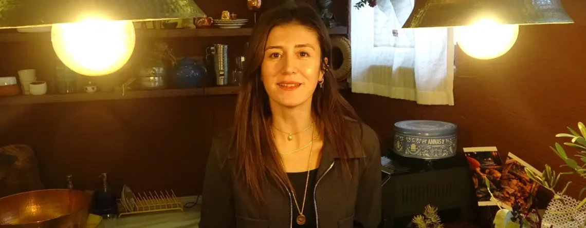 Bakır avizelerin aydınlattığı, bakır kaplar ve bitkilerle dolu bir atölyede gülümseyen bir kadın