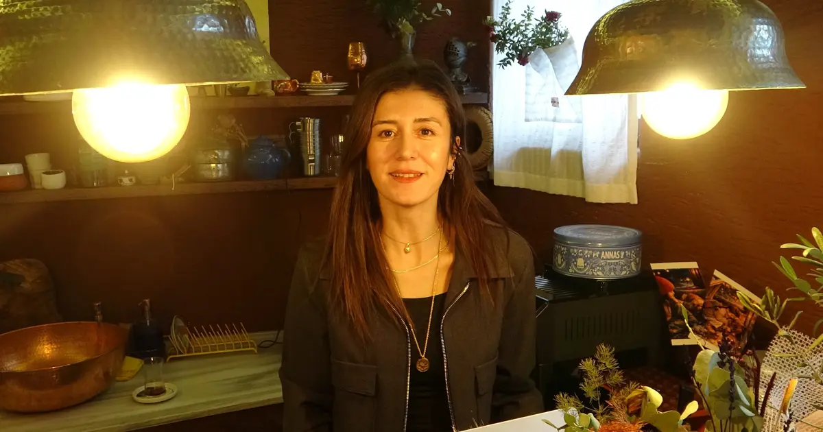 Bakır avizelerin aydınlattığı, bakır kaplar ve bitkilerle dolu bir atölyede gülümseyen bir kadın