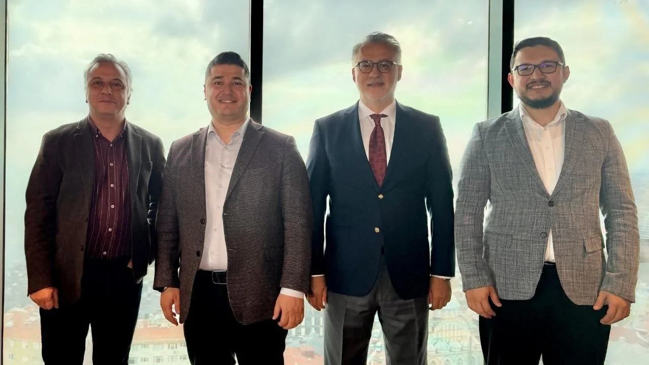 Yüksek bir binada büyük cam pencere önünde yan yana poz veren takım elbiseli dört adam