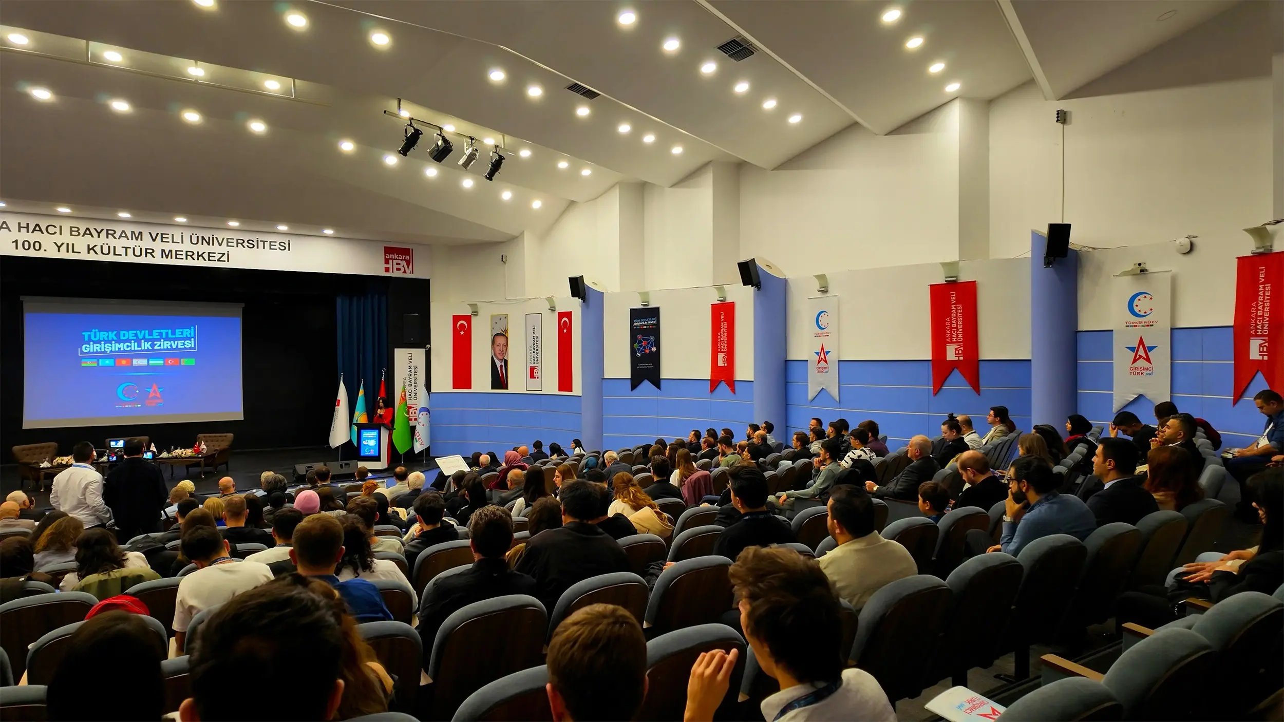 Ankara Hacı Bayram Veli Üniversitesi konferans salonunda sahnedeki ekranı izleyen kalabalık dinleyiciler