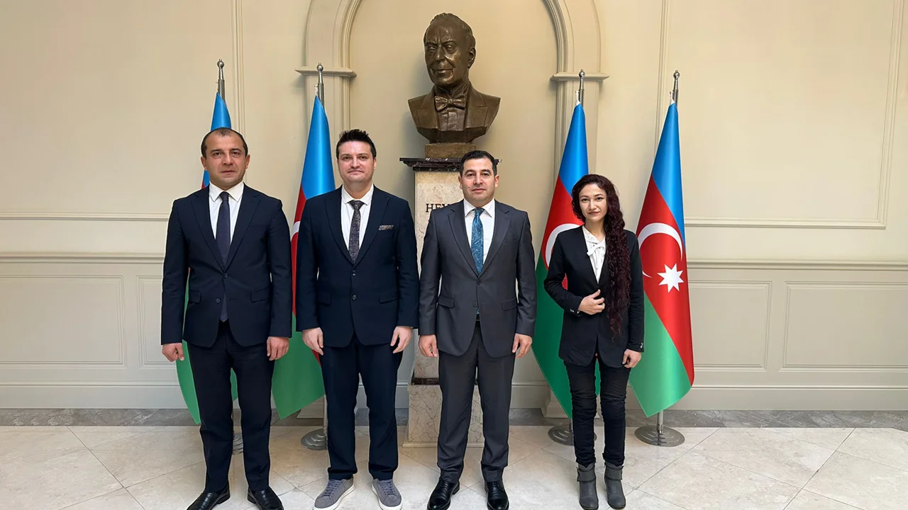 Azerbaycan bayrakları ve büst önünde, büyükelçilik salonunda yan yana poz veren üç adam ve bir kadın