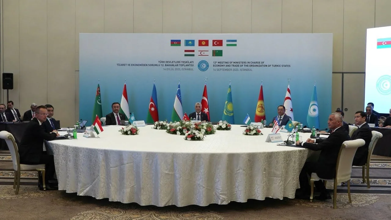 Türk devletlerinin bayraklarıyla süslü, beyaz örtülü yuvarlak masa etrafında toplanan heyetler