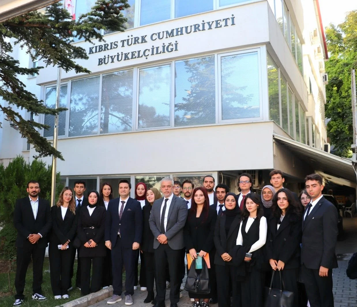 “Kıbrıs Türk Cumhuriyeti Büyükelçiliği” yazılı bina önünde toplu poz veren, koyu renk takım elbiseli genç bir grup