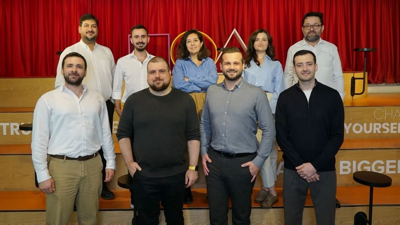 Kırmızı perdeli bir sahnede, basamaklarda iki sıra halinde poz veren on kişilik ekip