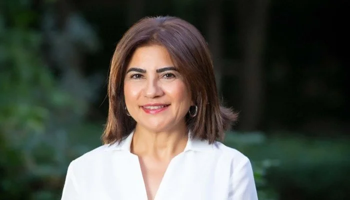 Yeşil, doğal bir arka plan önünde beyaz gömlekli, gülümseyen kısa saçlı bir kadın