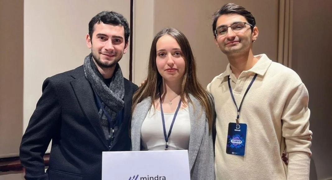 Mindra yazılı bir belge tutan, yaka kartlı iki genç adam ve bir genç kadın